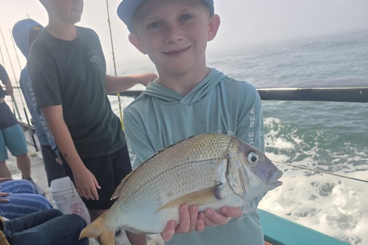 Child holding a fish on a boat with ocean in the background.