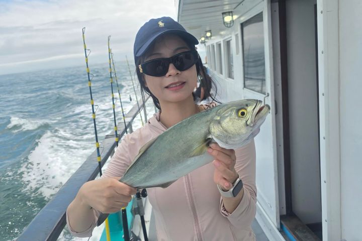 Person on a boat holding a fish, ocean in the background, wearing a cap and sunglasses.