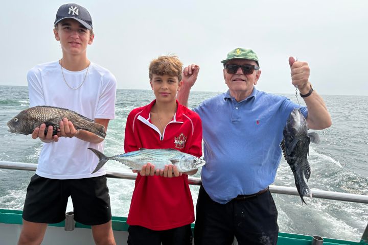 Three people on a boat holding fish, ocean in the background.