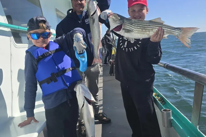 Three people on a boat holding freshly caught fish with the ocean in the background.