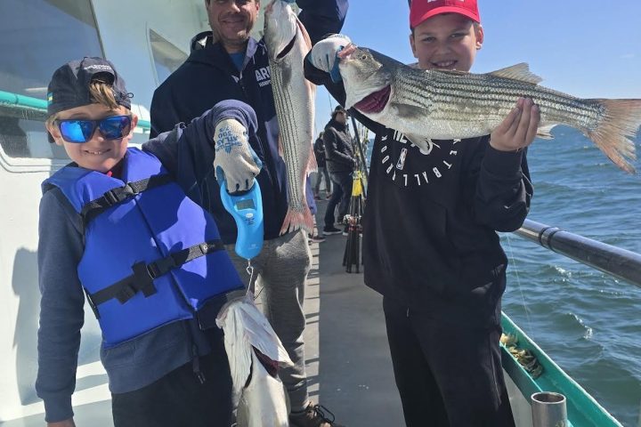 Three people on a boat holding freshly caught fish with the ocean in the background.