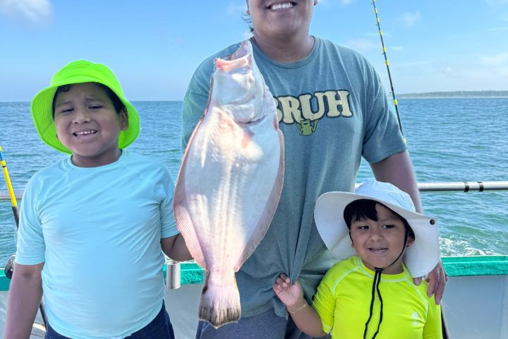 Three people on a boat holding a fish, smiling under a clear blue sky.