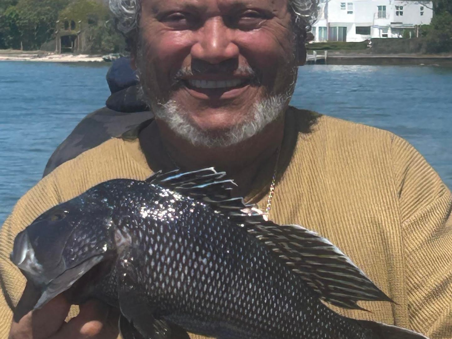 Man holding a large fish by the water on a sunny day.