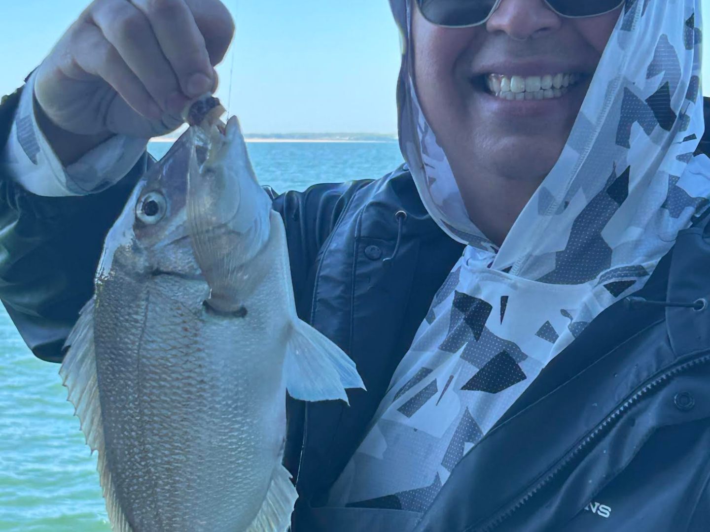 Person smiling, holding a fish on a line near a body of water.
