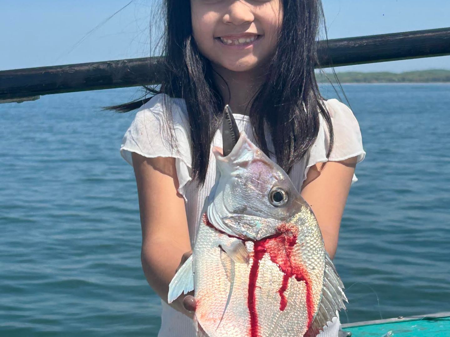Girl holding a large fish on a boat with a lake in the background.