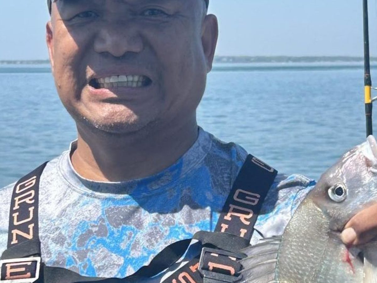 Man in fishing gear holding a fish on a boat.