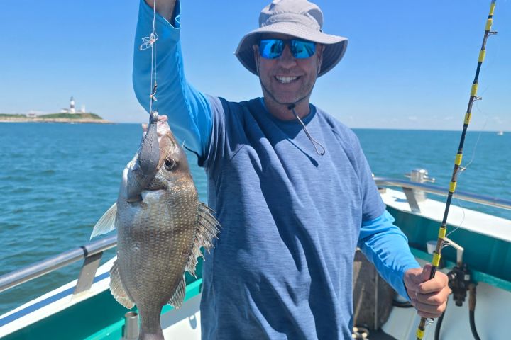 Man holding a fish on a boat, wearing a hat and sunglasses.