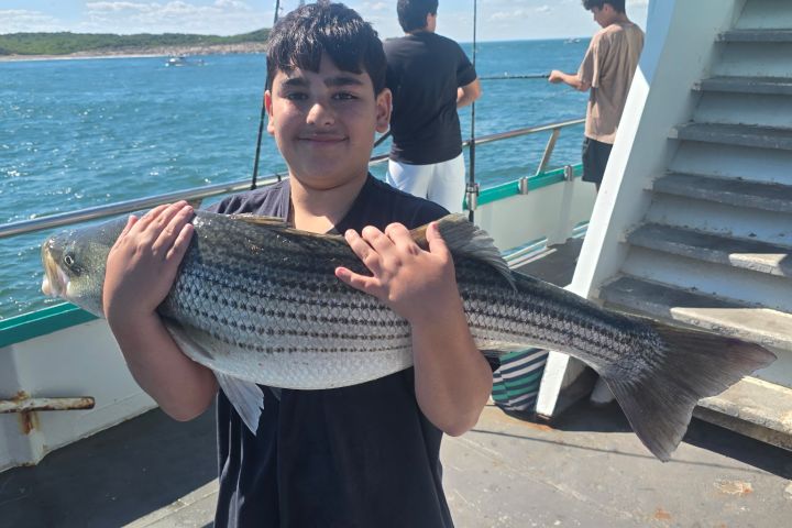 Boy on boat holding a large fish, with ocean in background.