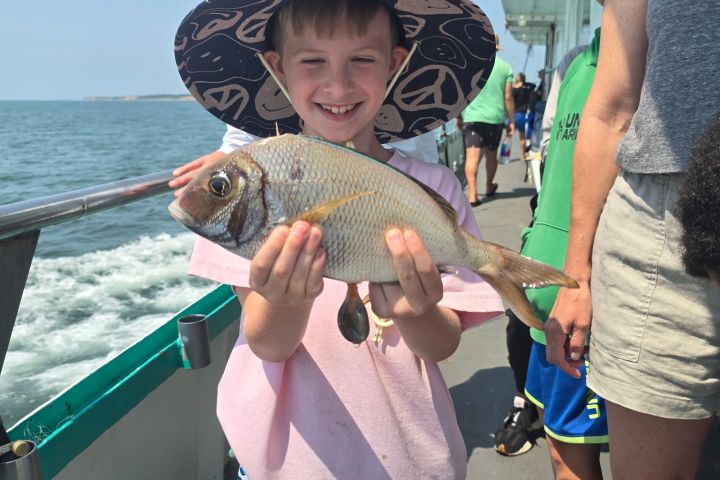 Smiling child on boat holding a fish, wearing a large straw hat.