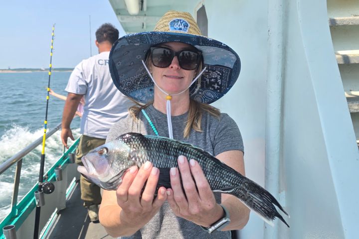 Woman on boat holding a fish with ocean in the background.
