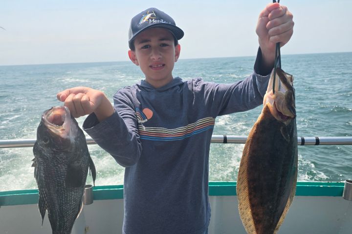 Boy holding two fish on a boat with ocean in the background.