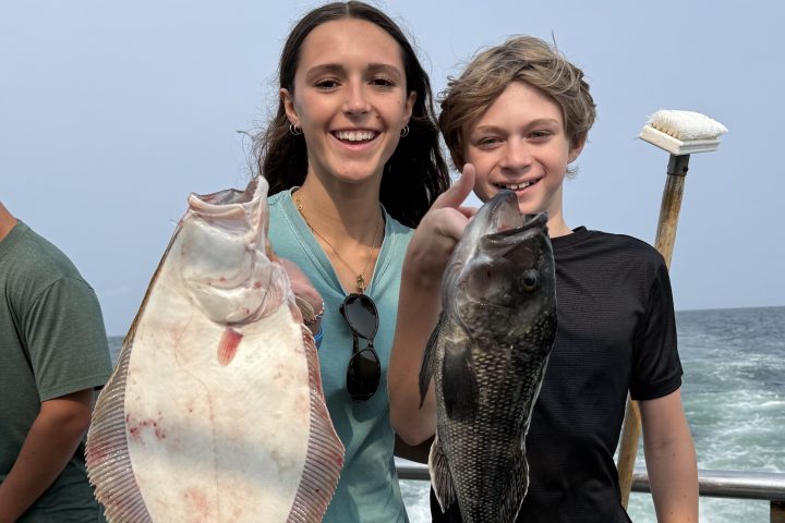 Two people smiling, each holding a large fish on a boat.