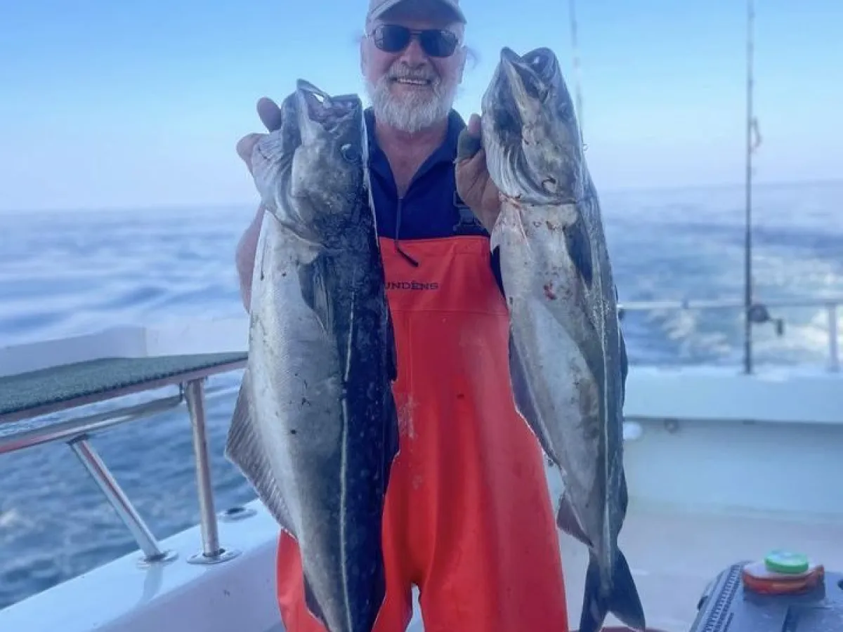 Person in orange overalls holding two large fish on a boat.