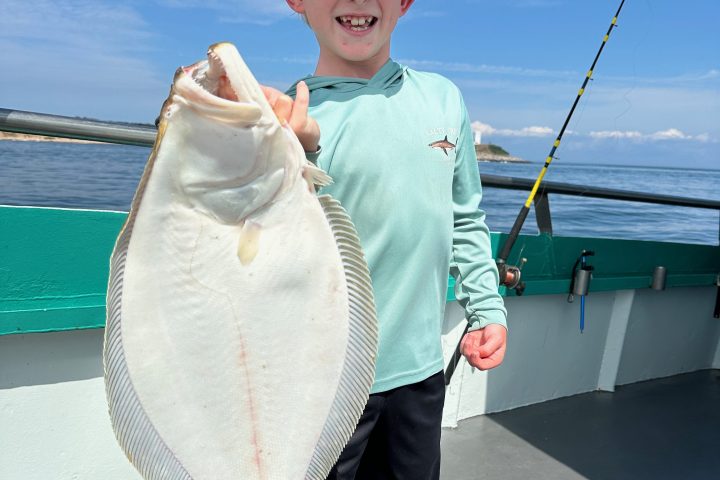 Child on a boat holding a large flat fish, wearing a hat and smiling.