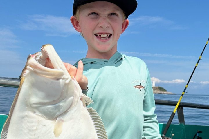 Child on a boat holding a large flat fish, wearing a hat and smiling.