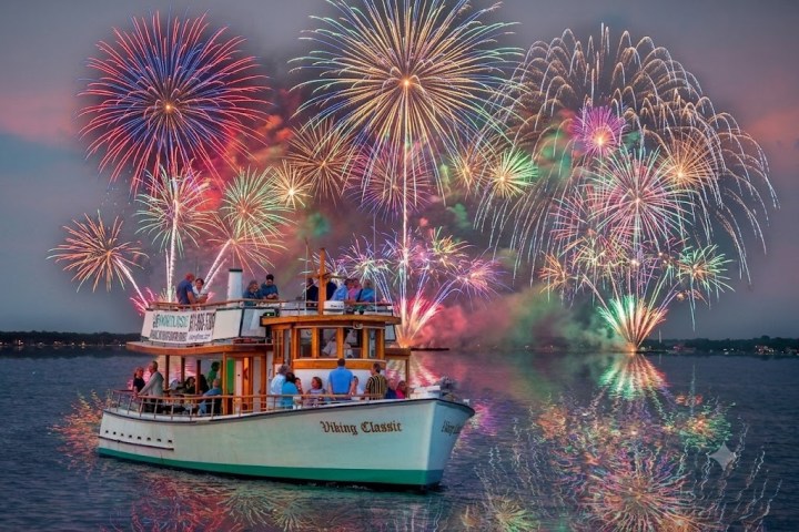 Boat on water with colorful fireworks in the sky at dusk.