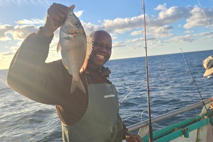 Person on a boat holding a fish under a clear blue sky with fishing rods in the background.