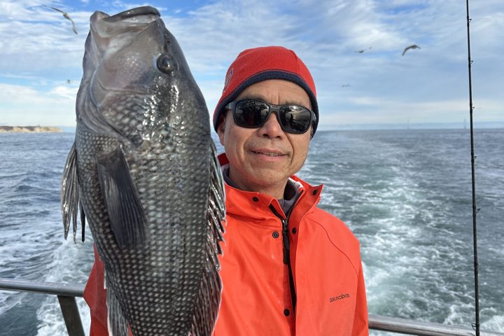 Person in red jacket holds large fish on boat with ocean backdrop.