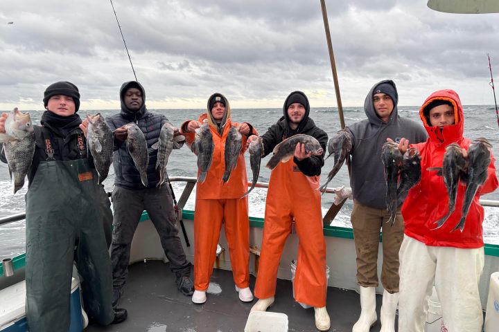 Six people holding fish on a boat with cloudy sky.