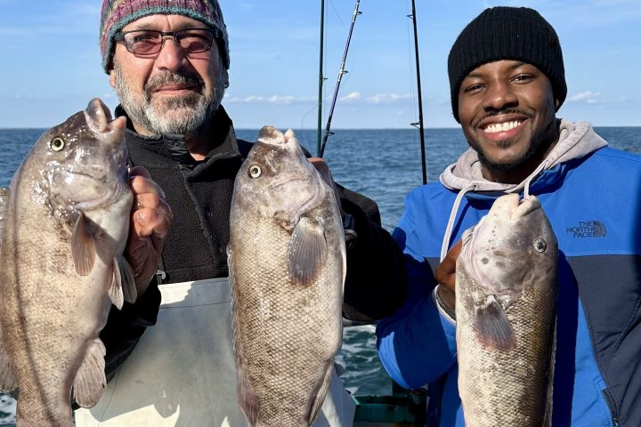Two men on a boat holding large fish, smiling at the camera.