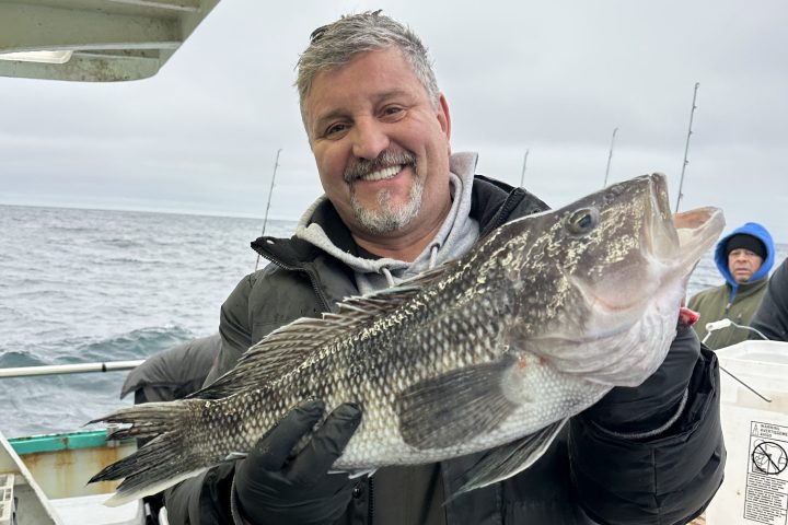 Person on a boat holding a large fish, smiling at the camera, with a cloudy sky in the background.