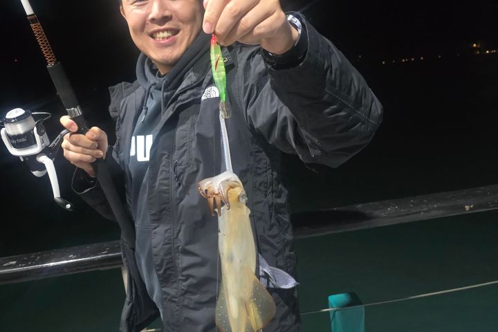 Person smiling and holding a squid caught on a fishing rod at night on a boat.