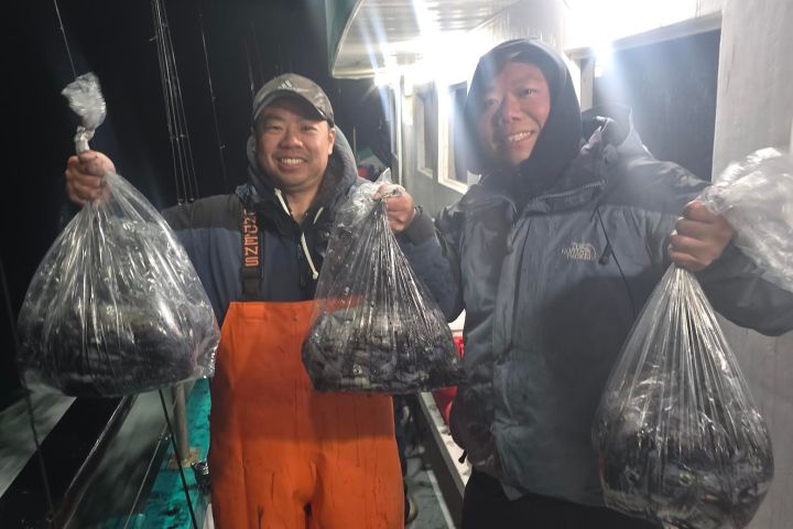 Two people on a boat holding bags of fish at night.