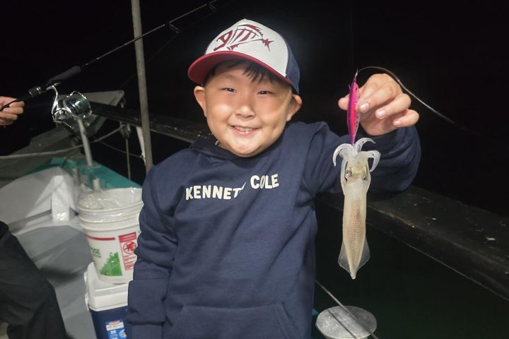 Child on a boat smiling and holding a small squid at night.