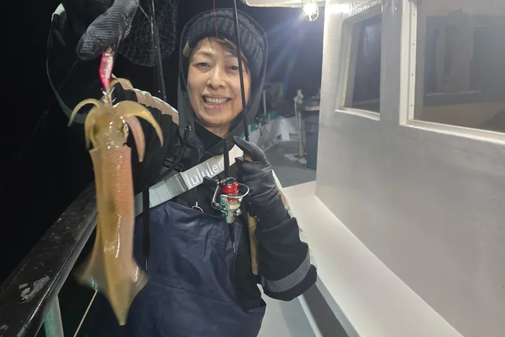 Person on a boat at night smiling and holding a squid with fishing gear.