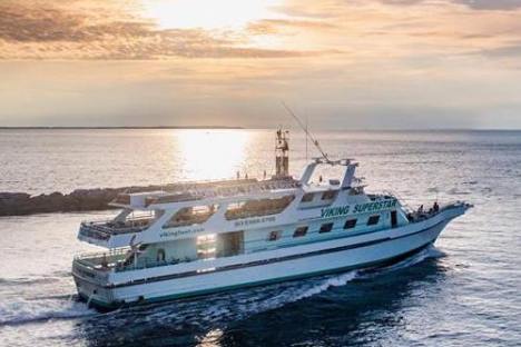 Ferry on ocean at sunset with cloudy sky and sun reflection on water.