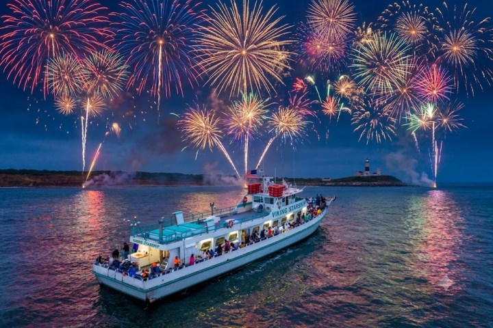 Boat on water with colorful fireworks in the night sky.