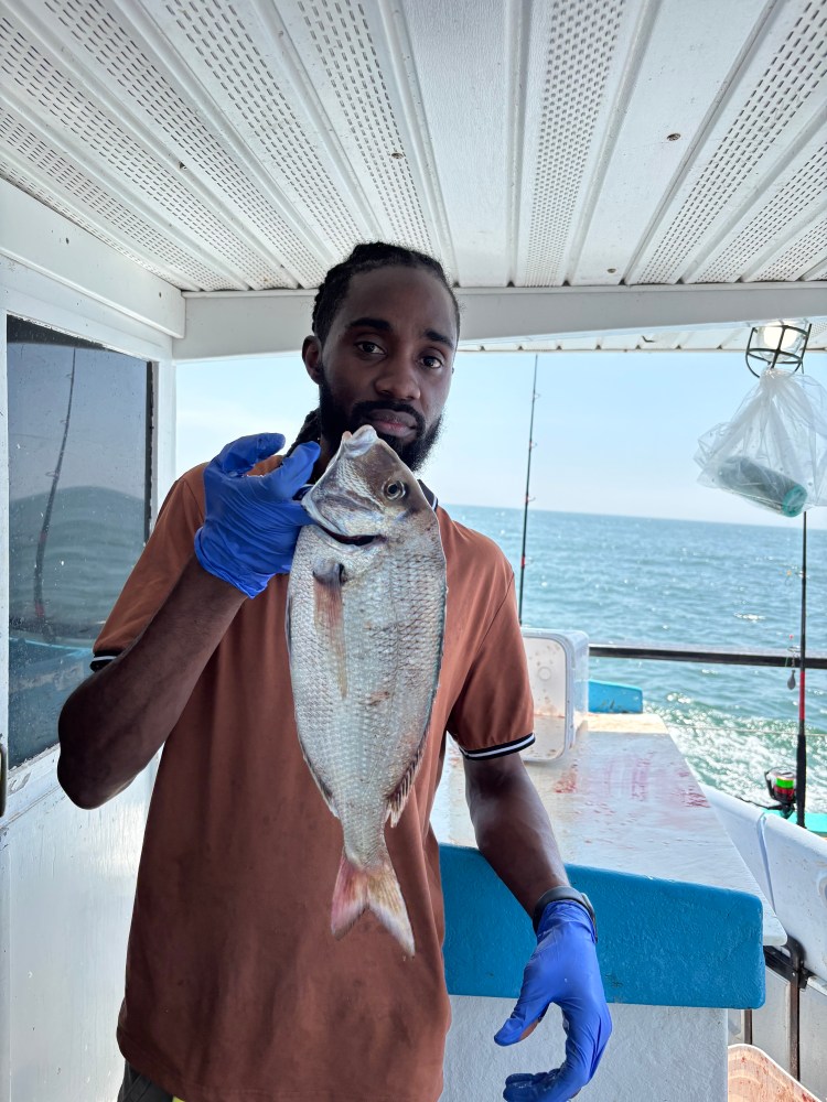 Person holding a fish on a boat with ocean in the background.