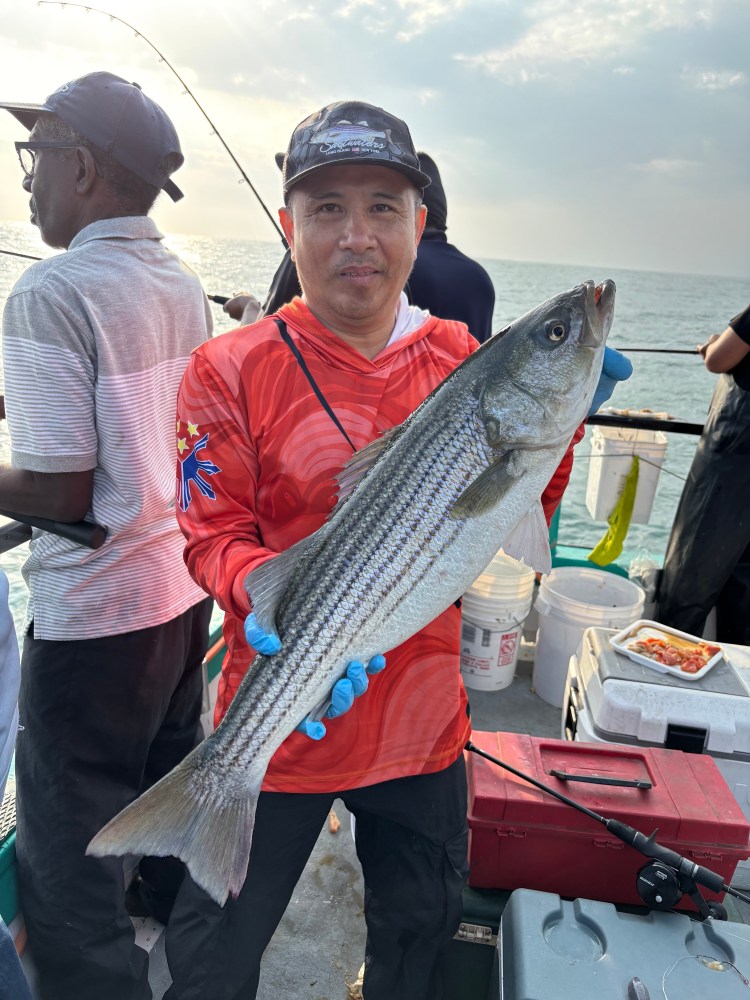 Man holding a large fish on a boat with others fishing nearby.